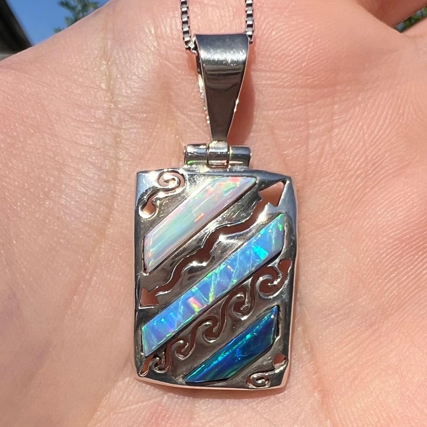 Close-up of a men's 950 silver lab-created opal necklace, shown in the sunlight in a hand.