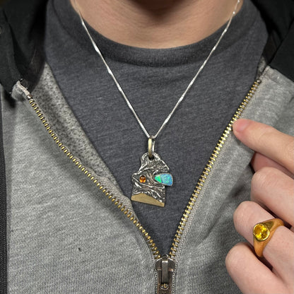 Close-up of a person wearing a men's opal and amber pendant in sterling silver by Starborn Creations against a dark shirt beneath a hoodie.