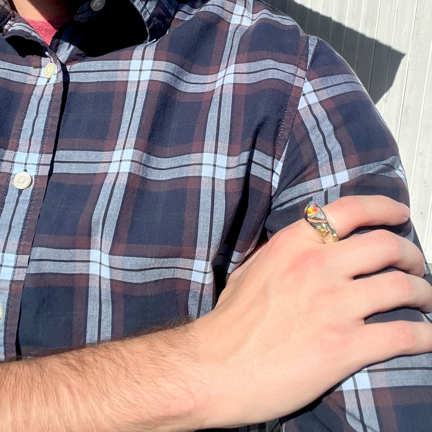 Hand resting on shoulder while wearing a men's boulder opal and gold nugget ring.  The opal flashes red and orange colors in sunlight.