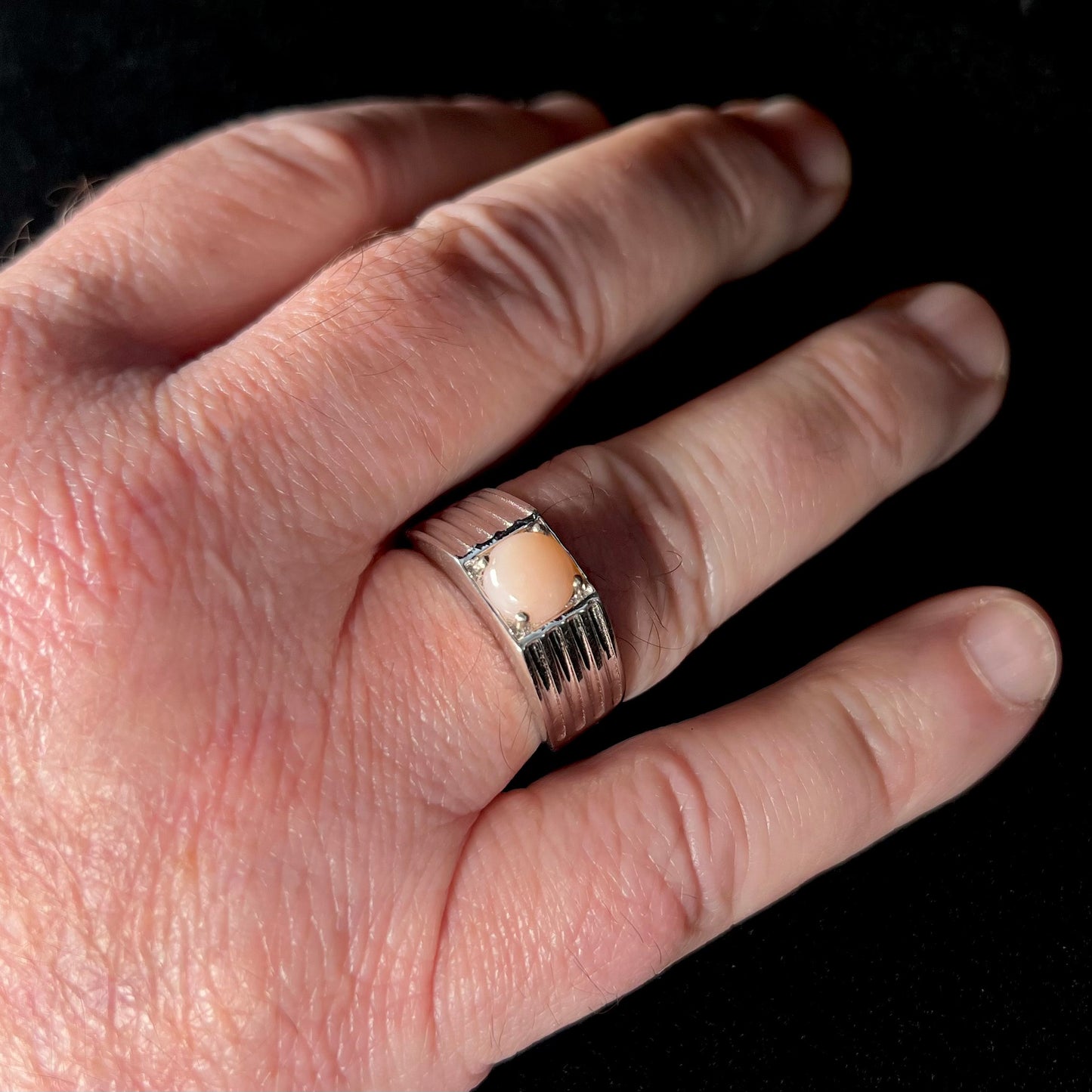 Man's hand wearing a men's sterling silver pink Peruvian opal ring, size 12