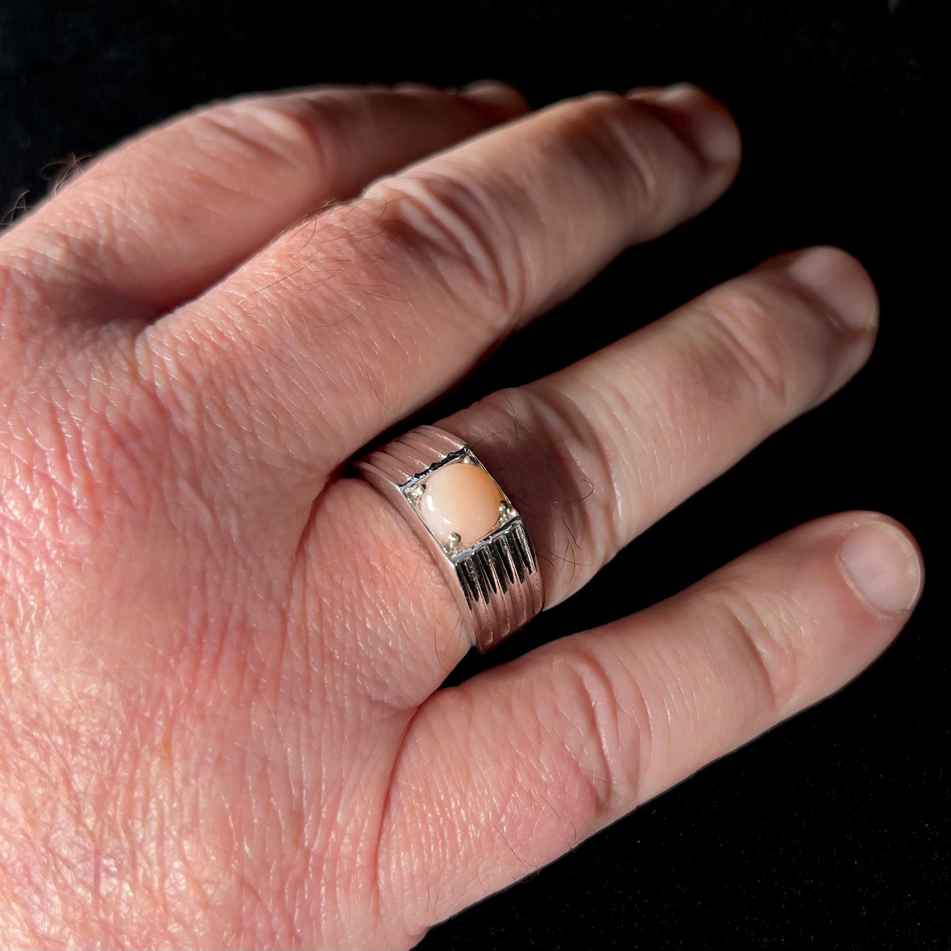 Man's hand wearing a men's sterling silver pink Peruvian opal ring, size 12