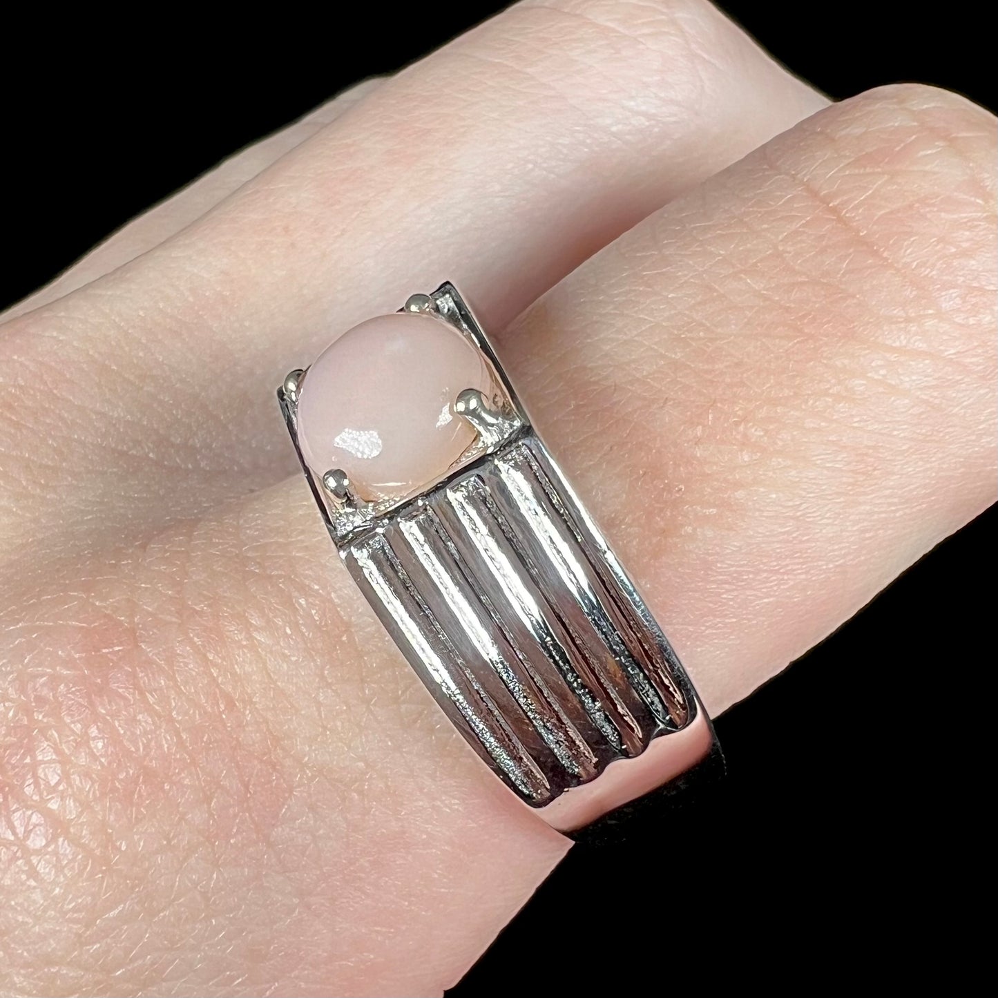 Angled close-up of men's pink opal solitaire ring in silver on finger