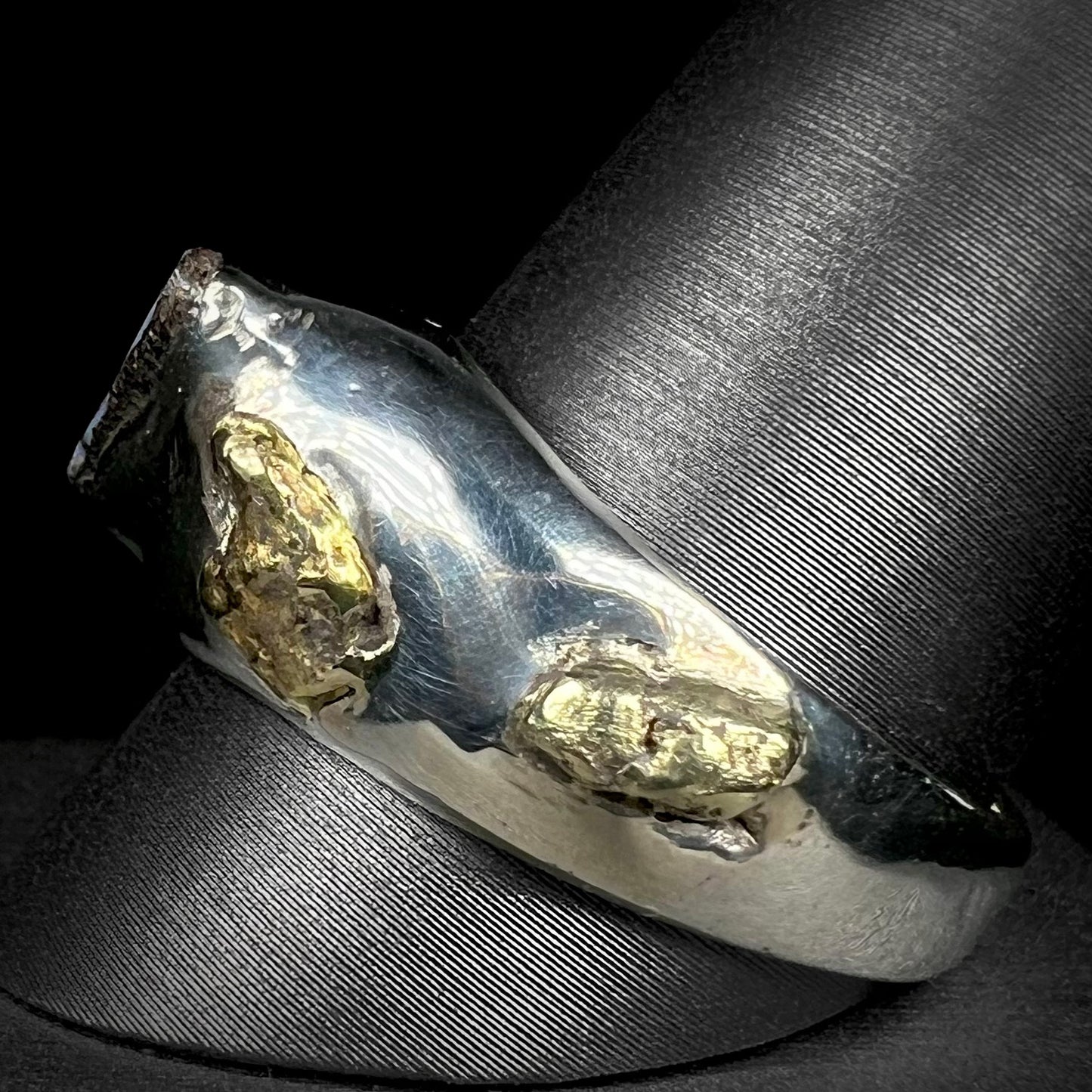 A men's size 12 sterling silver ring accented with two placer gold nuggets shown from the side angle on a ring display.