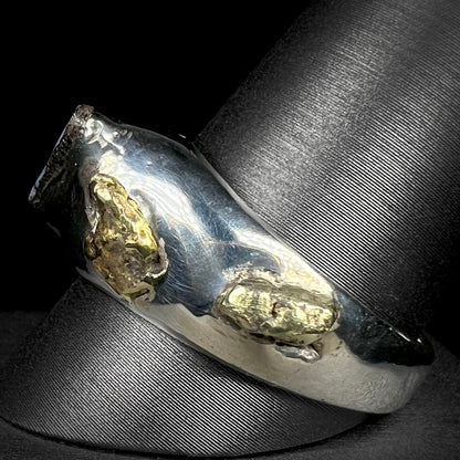 A men's size 12 sterling silver ring accented with two placer gold nuggets shown from the side angle on a ring display.