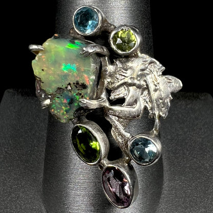 A silver men's ring set with rough Virgin Valley opal and gems with a female figure design, shown from the front.