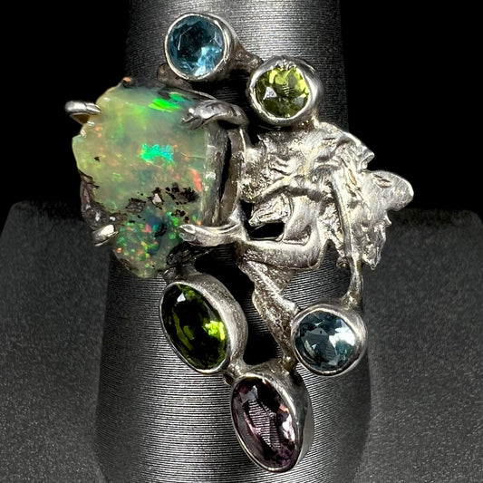 A silver men's ring set with rough Virgin Valley opal and gems with a female figure design, shown from the front.
