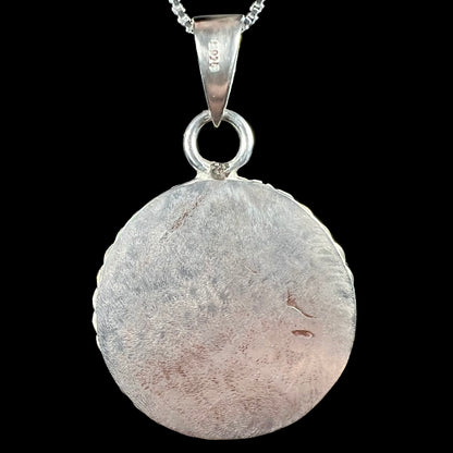 Back side of a handmade round sterling silver medallion necklace, shown against a black backdrop.