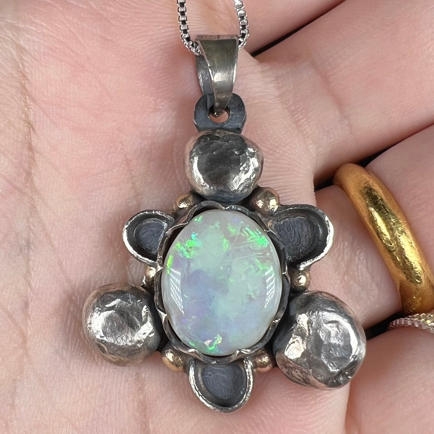 Close-up of a men's rustic two-tone sterling silver and gold Australian opal pendant, held in a hand.