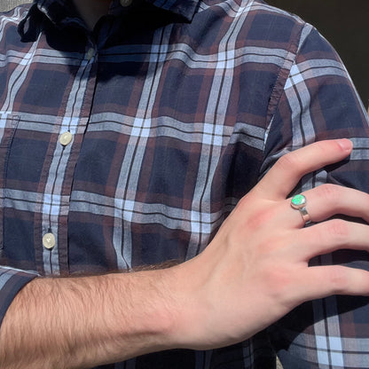 Close-up of person in sunlight resting hand on opposing shoulder while wearing a men's sterling silver Australian opal ring with a green flash of color.