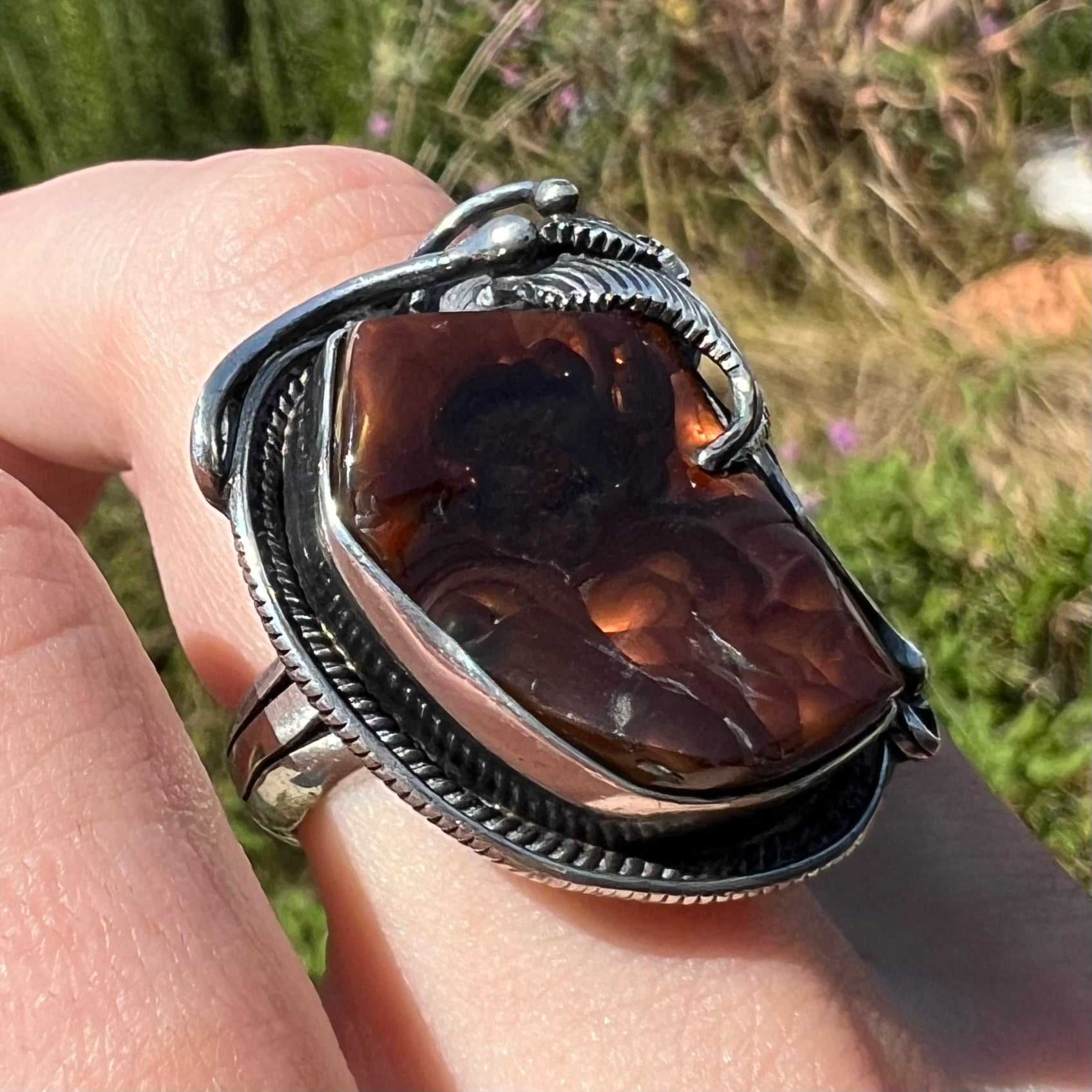 Angled sunlit view of a men's silver, Southwest-style fire agate ring worn on a finger.