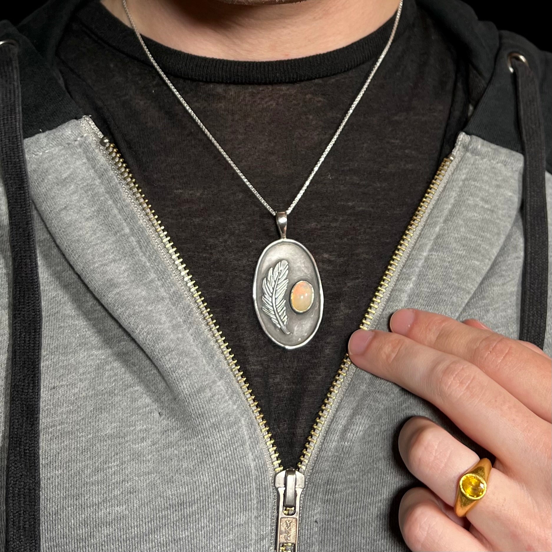 Man wearing a sterling silver Ethiopian fire opal and feather design necklace around neck inside of hoodie against dark shirt.