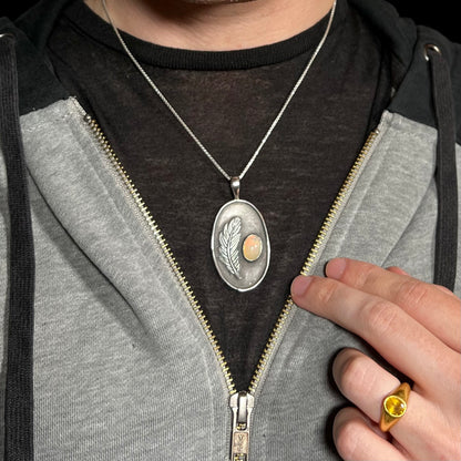 Man wearing a sterling silver Ethiopian fire opal and feather design necklace around neck inside of hoodie against dark shirt.