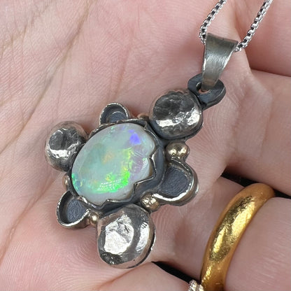 A men's rustic two-tone sterling silver and gold Australian opal pendant, shown from an angle in a hand.