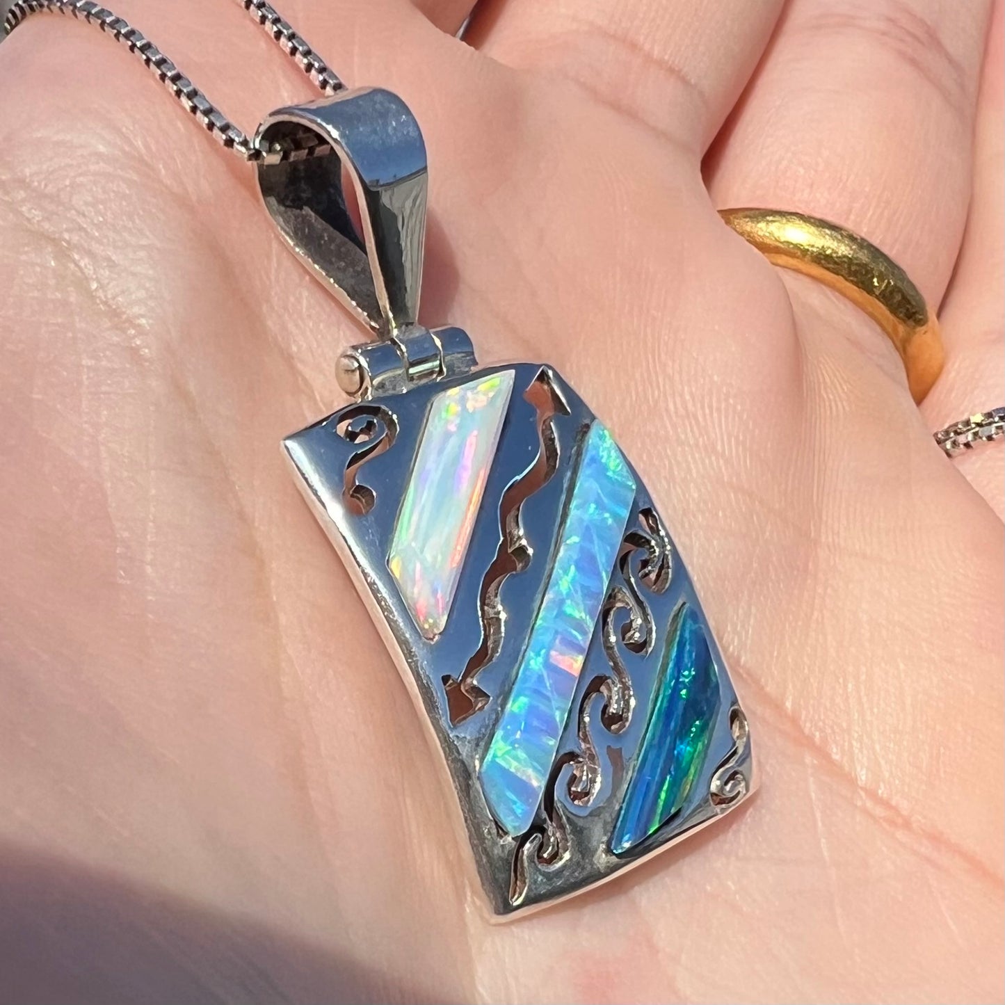 Angled close-up of a men's 950 silver lab-created opal necklace in sunlight, held in a hand.
