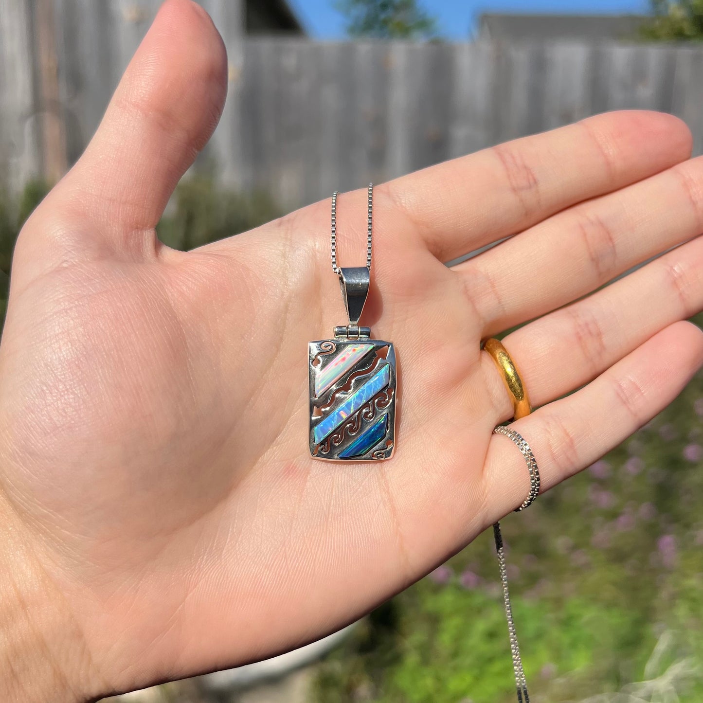 A men's 950 silver lab-created opal necklace, shown in a hand in outdoor sunlight.