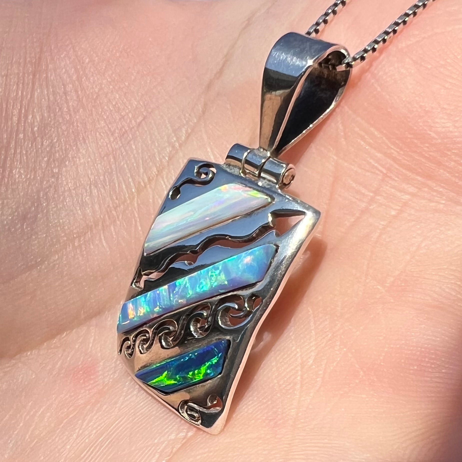 A men's 950 silver lab-created opal necklace shown in the sunlight from a close-up angle, held in a hand.