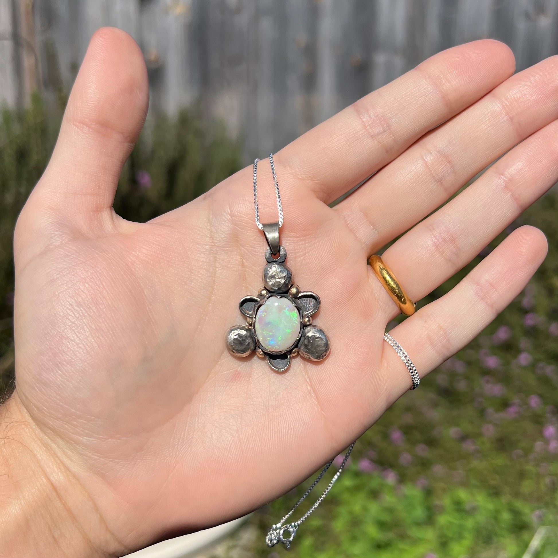 A men's rustic two-tone sterling silver and gold Australian opal pendant, shown in a hand in sunlight.