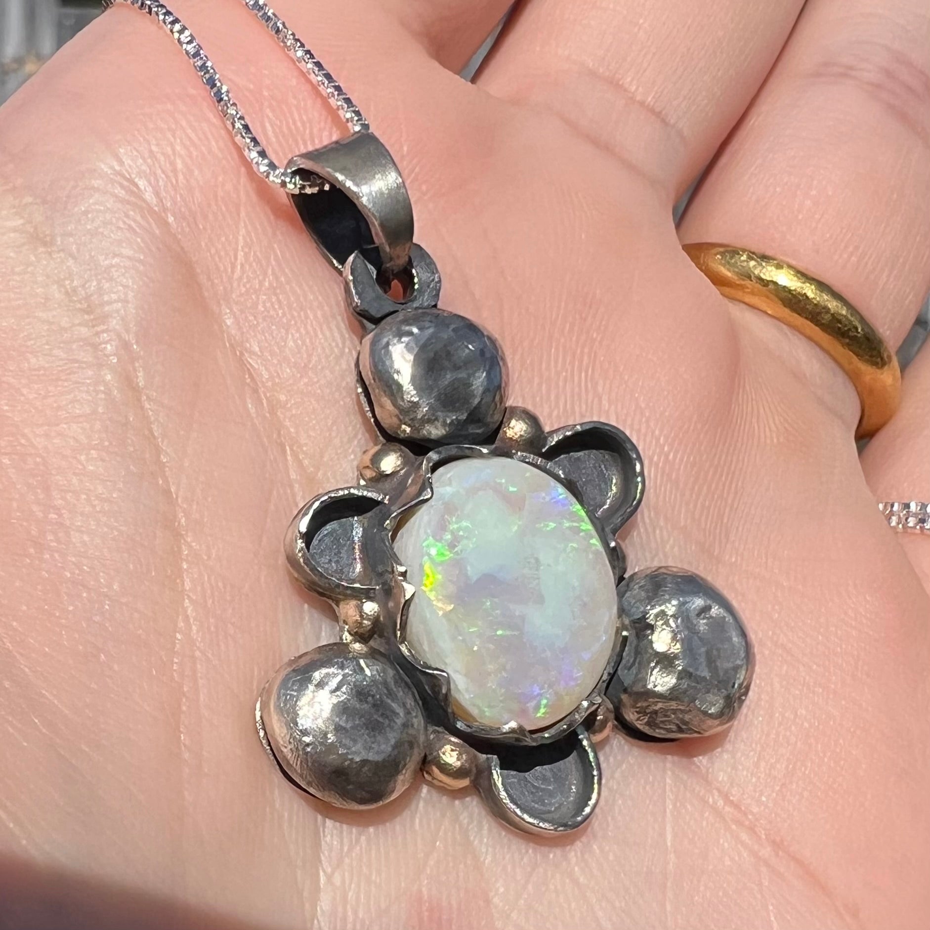 Close-up angled view of a men's rustic two-tone sterling silver and gold Australian opal pendant in the sunlight.