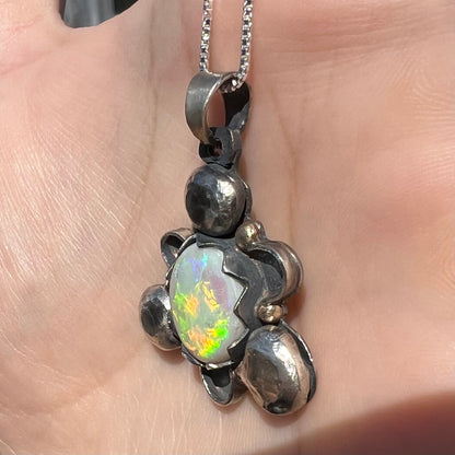 Angled close-up of a men's sterling silver opal pendant in the sunlight; the opal has orange and green colors.
