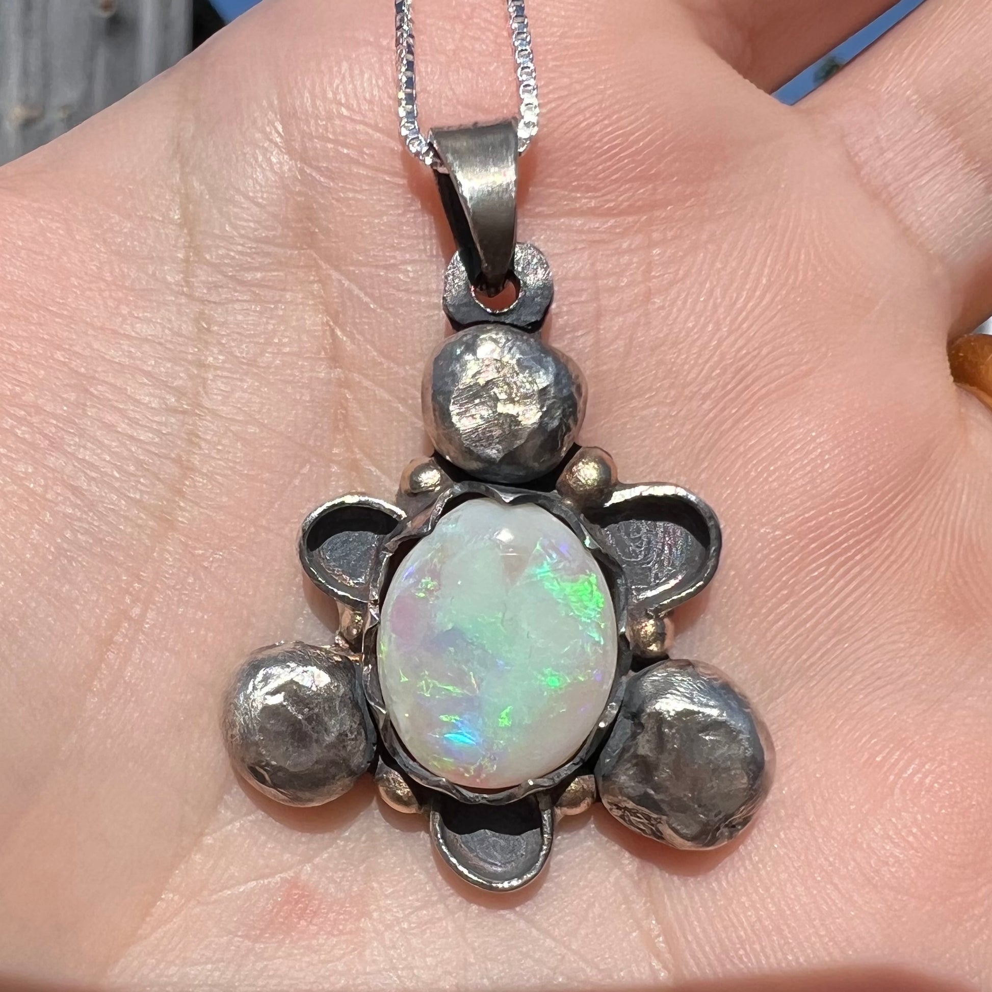 A men's rustic two-tone sterling silver and gold Australian opal pendant, shown close-up in a hand in sunlight.