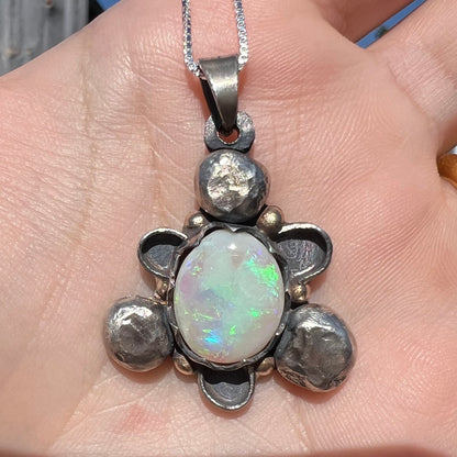 A men's rustic two-tone sterling silver and gold Australian opal pendant, shown close-up in a hand in sunlight.
