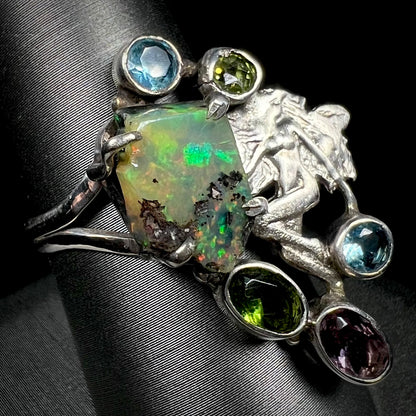A silver men's ring set with rough Virgin Valley opal and gems with a female figure design shown from an angle.