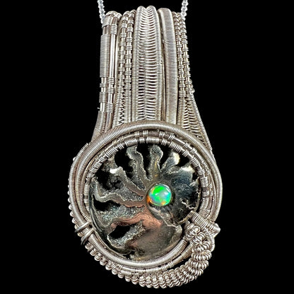 Men's rustic silver wire wrapped pendant set with pyritized ammonite shell fossil, accented by round Ethiopian fire opal, shown from front.