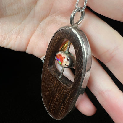A men's sterling silver dark brown wood pendant with a Mexican fire opal accent, shown from an angle in a hand close-up.