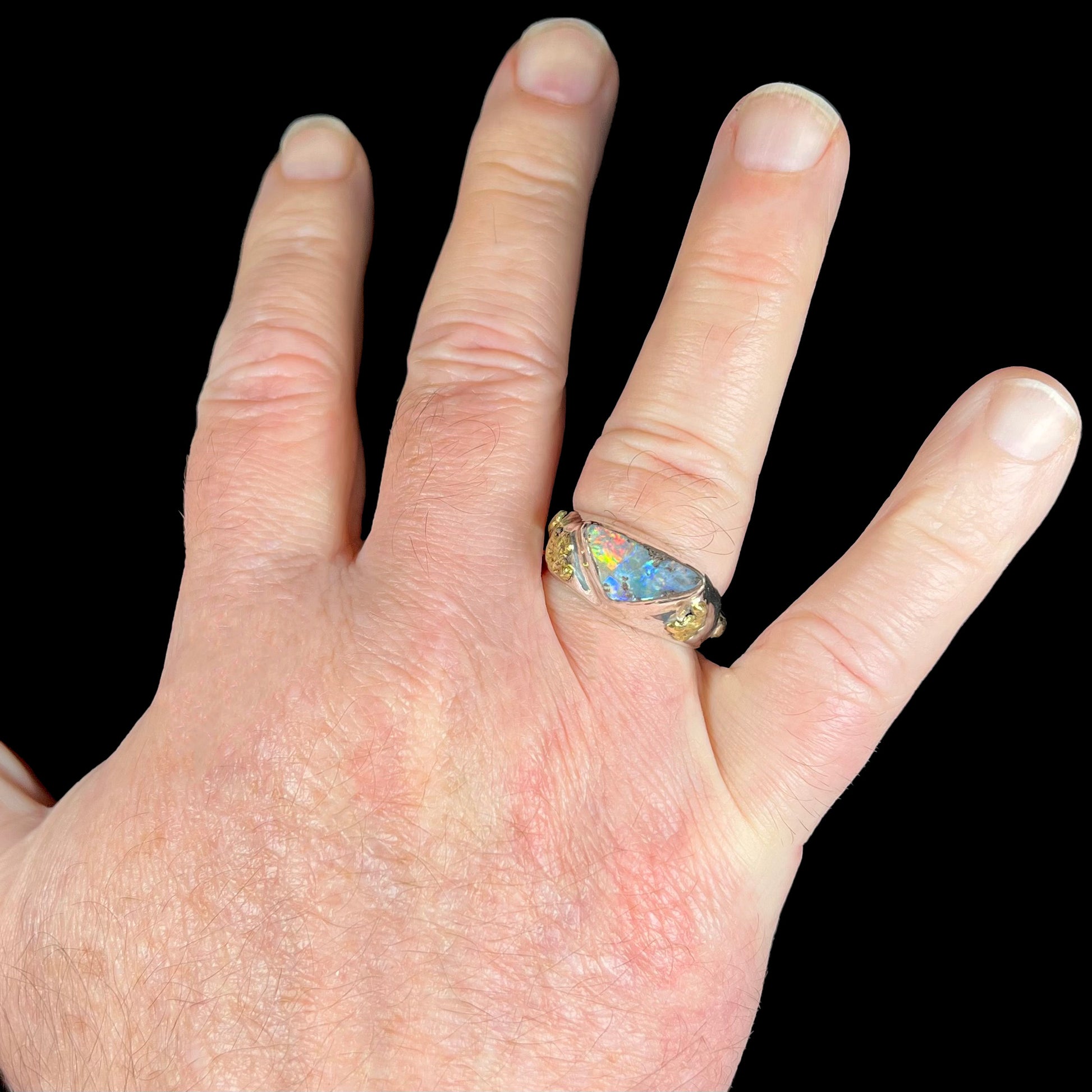A size 12 men's sterling silver Australian boulder opal ring shown on a man's open hand against a black background.