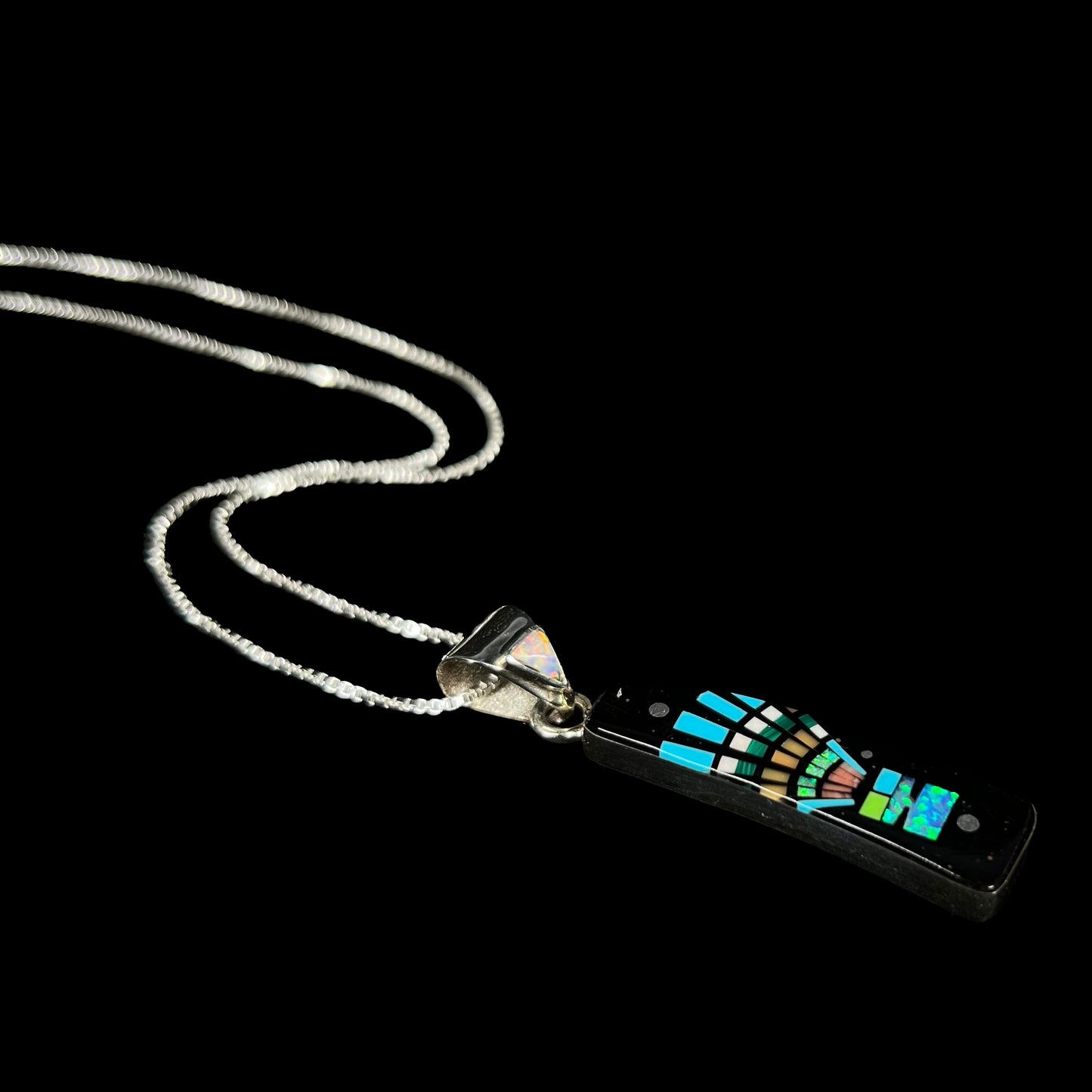 Men's Southwest-inspired sterling silver opal in onyx inlay necklace shown from angle laying against black background.