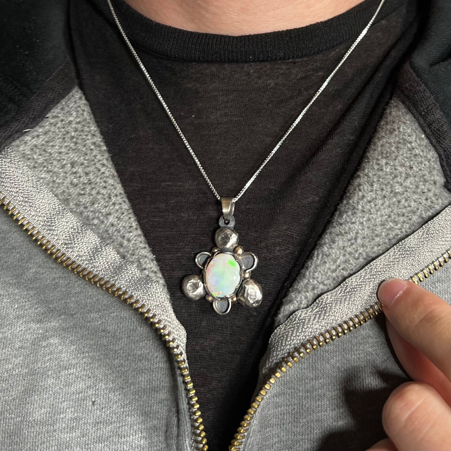A men's rustic two-tone sterling silver and gold Australian opal necklace, worn around a neck on a dark shirt.