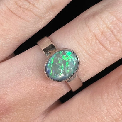 Close-up of a men's US size 7.75 sterling silver Australian opal solitaire ring, worn on a finger.  The opal has a bright bluish green flash of color under studio light.