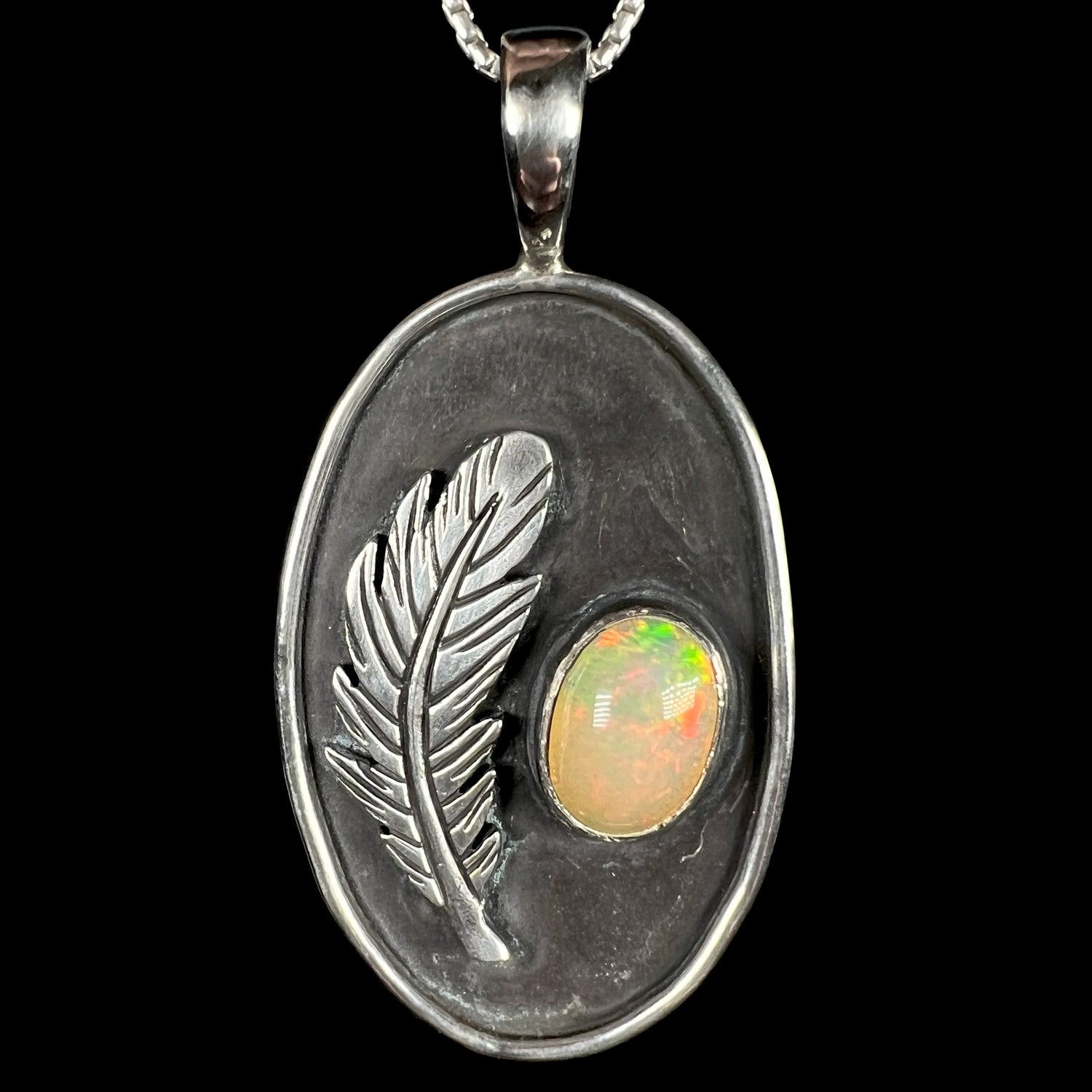 A men's sterling silver Ethiopian opal and feather design necklace by Austin Henderson of Serpent Stones Jewelry, shown against black background.