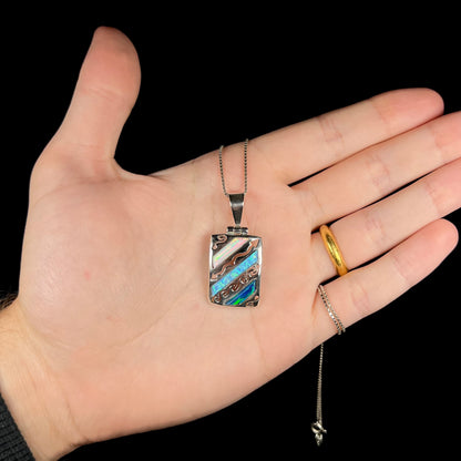 A men's 950 silver lab-created opal pendant, shown in a hand against a black background.