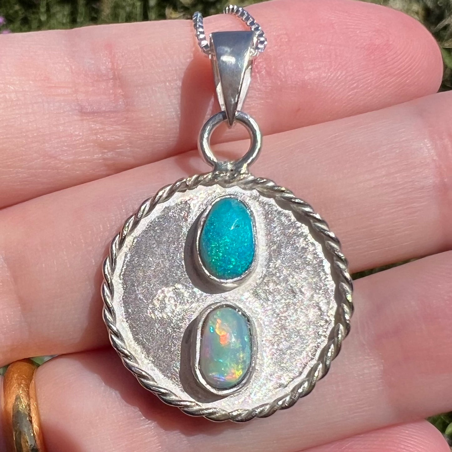 Close-up macro view of a textured sterling silver men's pendant set with two natural Australian opals, held in the sunlight.