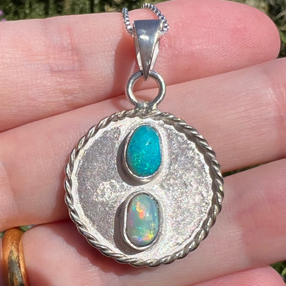 Close-up macro view of a textured sterling silver men's pendant set with two natural Australian opals, held in the sunlight.