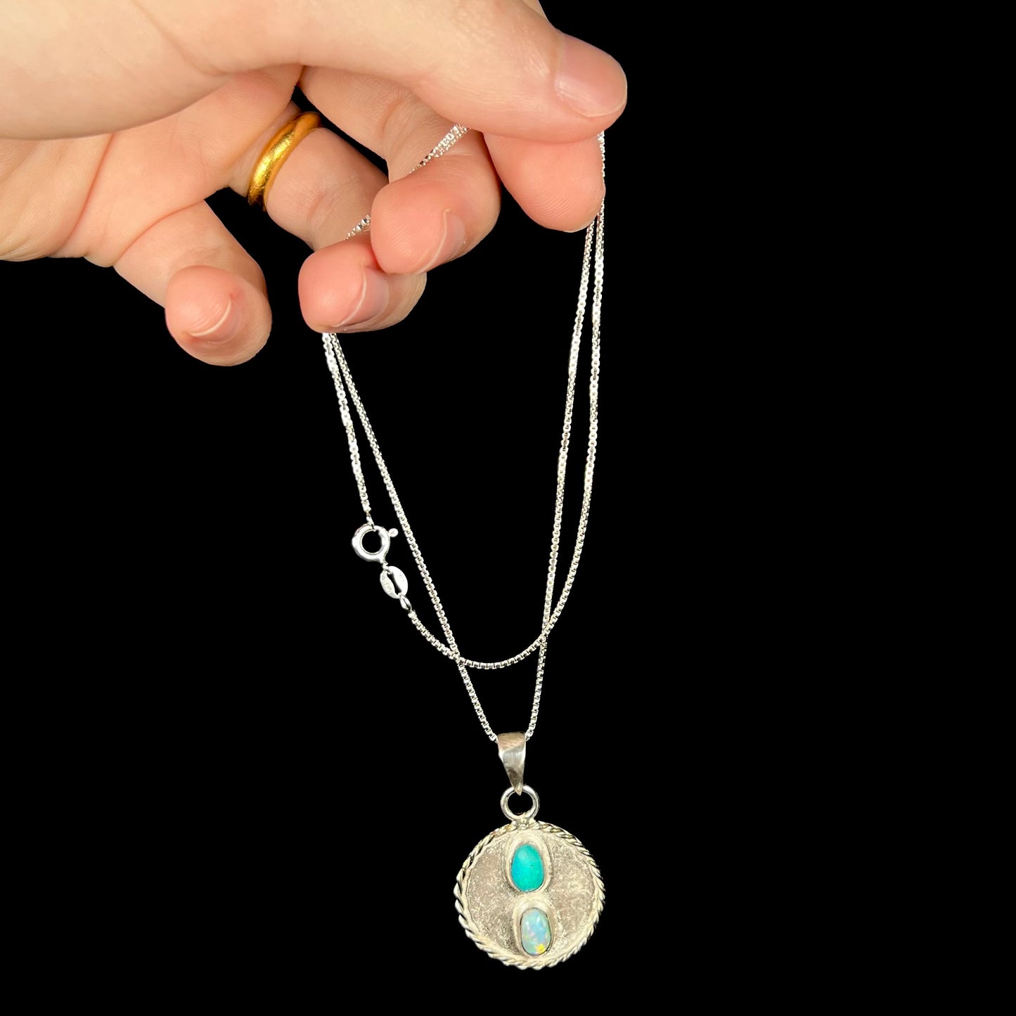 Hand dangling a men's two-stone Australian opal necklace made from sterling silver by its silver box chain.