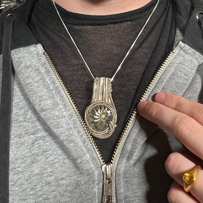Man wearing silver wire wrapped ammonite and opal necklace around neck inside of jacket against dark shirt.