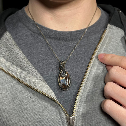 Close-up of a men's wire wrapped Australian boulder opal necklace worn around a person's neck against a dark shirt beneath a hoodie.