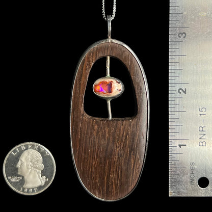 A large, 3.25 inch-long men's wood and Mexican matrix fire opal pendant in sterling silver shown next to a ruler and US quarter coin for scale.