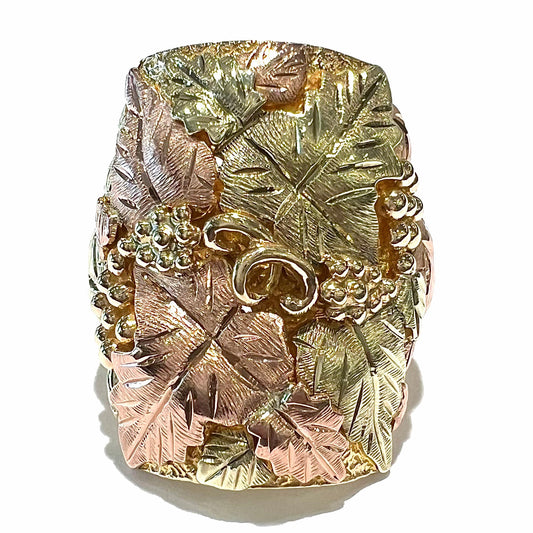 A men's solid gold ring.  The ring is Black Hills gold featuring a grapevine and leaf motif with rose and green gold designs.