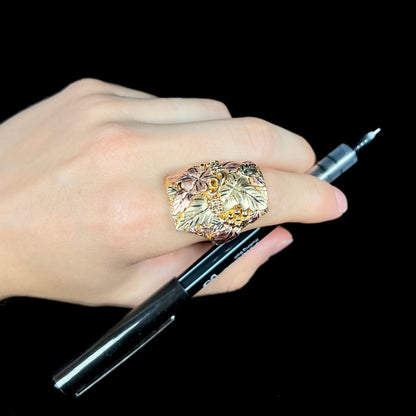 A men's solid gold ring.  The ring is Black Hills gold featuring a grapevine and leaf motif with rose and green gold designs.