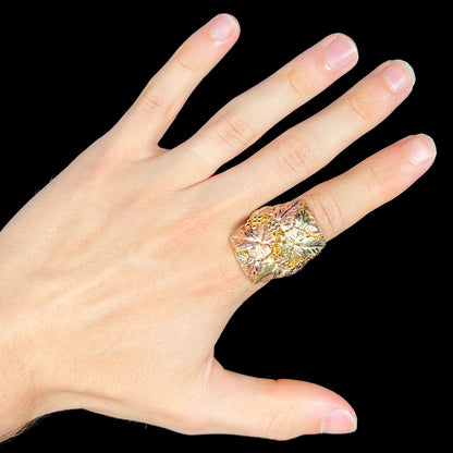 A men's solid gold ring.  The ring is Black Hills gold featuring a grapevine and leaf motif with rose and green gold designs.