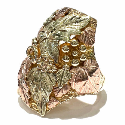 A men's solid gold ring.  The ring is Black Hills gold featuring a grapevine and leaf motif with rose and green gold designs.