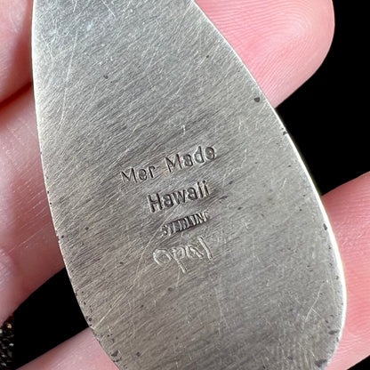 Close-up of the back side of a sterling silver pendant focused on the stamps "Mer Made Hawaii STERLING" and the etched word "Opal".