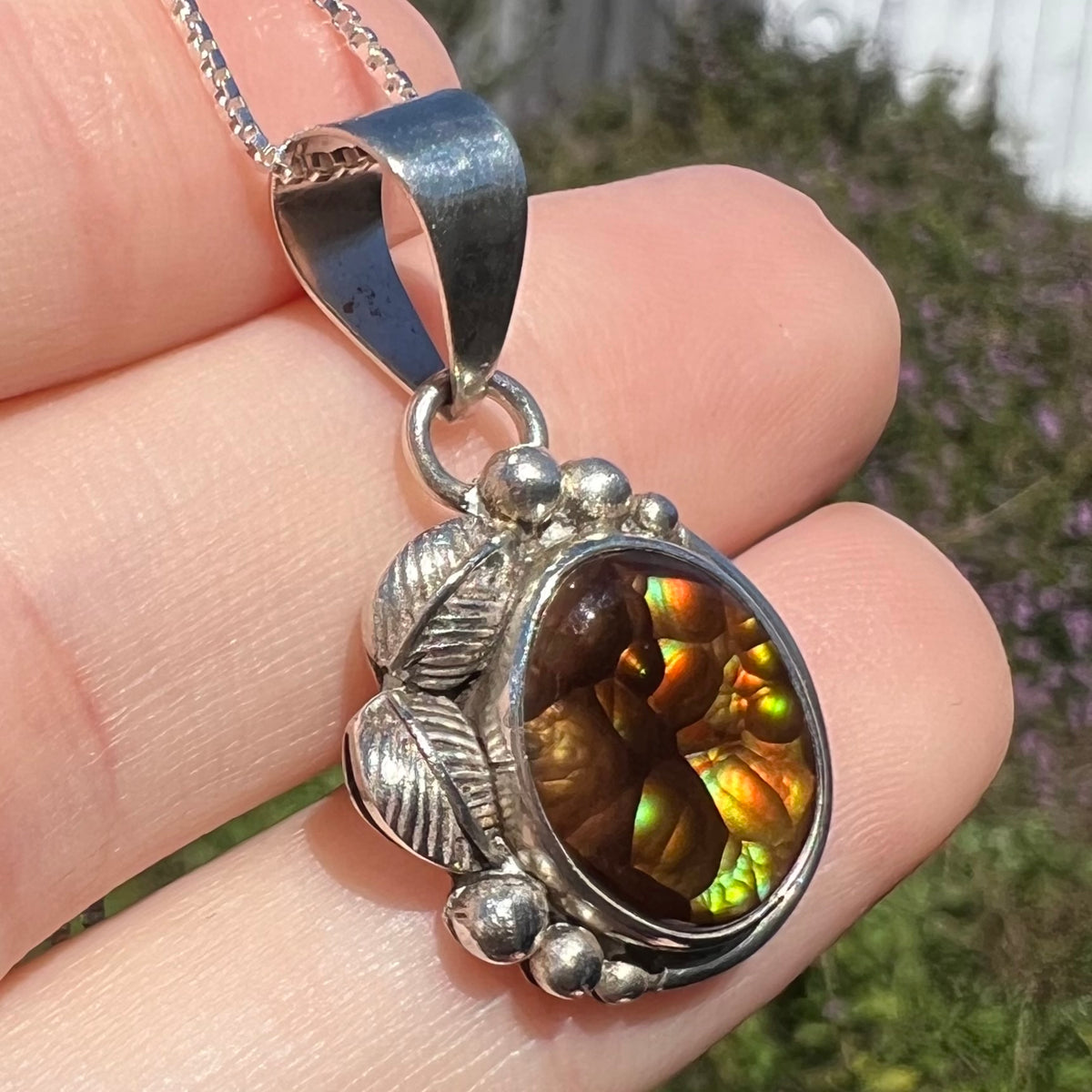 Angled macro view of Mexican fire agate pendant with silver leaf design, held in hand under sunlight.