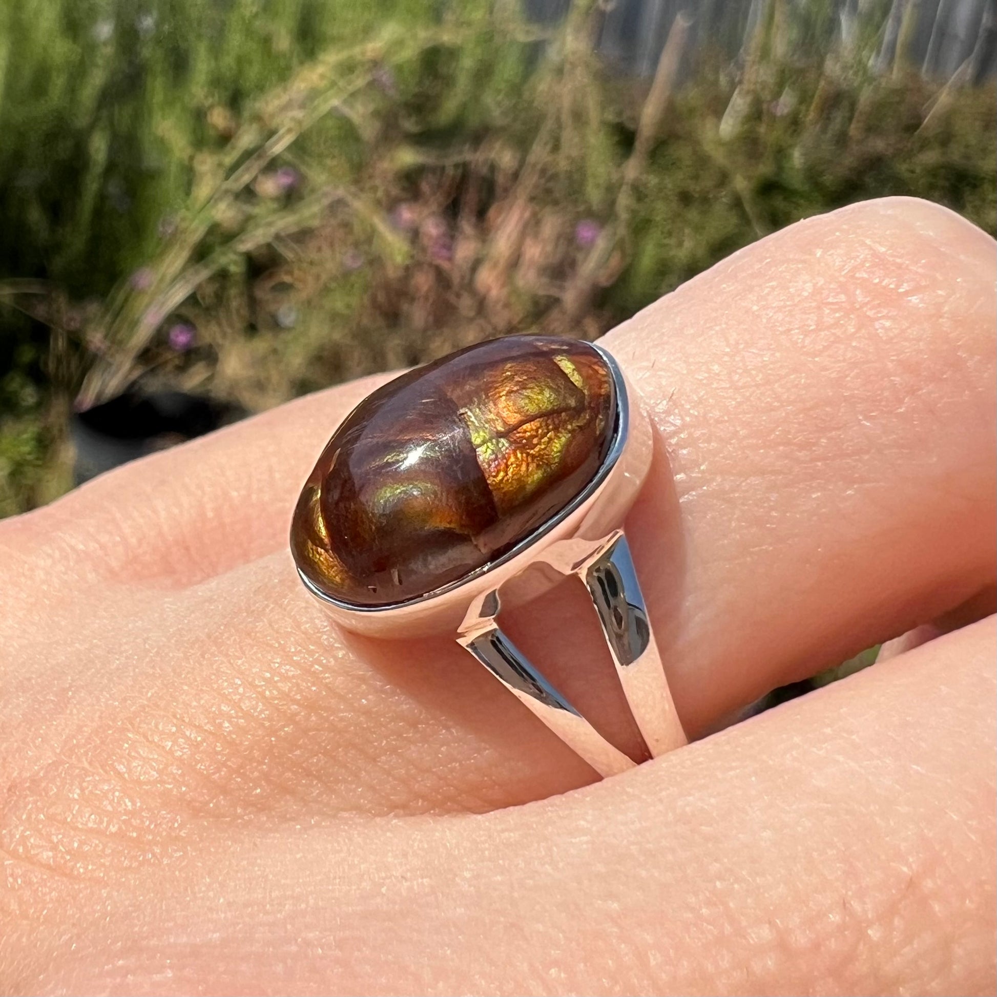 Close-up angled view of a sterling silver Mexican fire agate ring with a split shank worn on a finger.