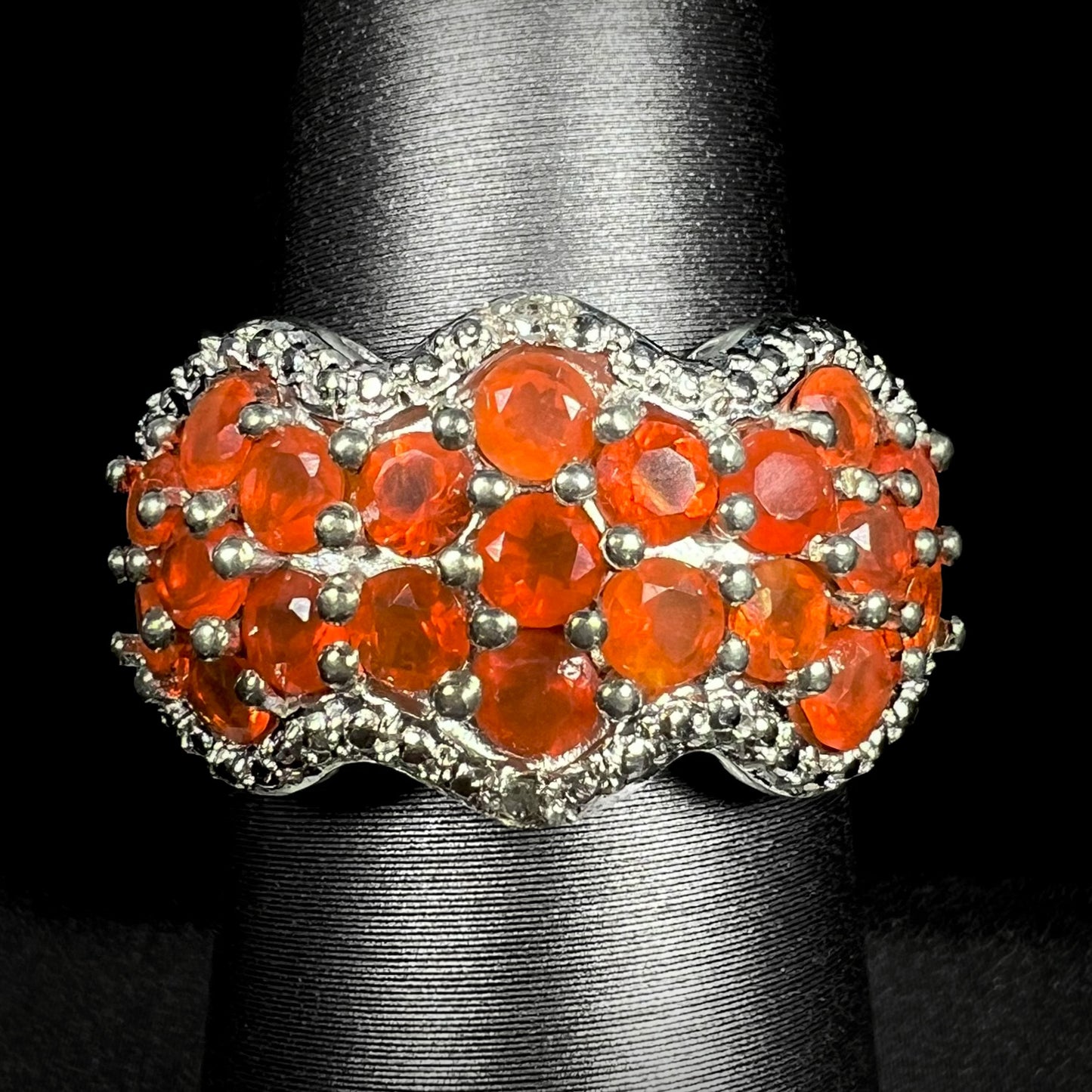 Front close-up of a Mexican fire opal cluster ring with diamond accents in sterling silver, shown on ring display against black background.