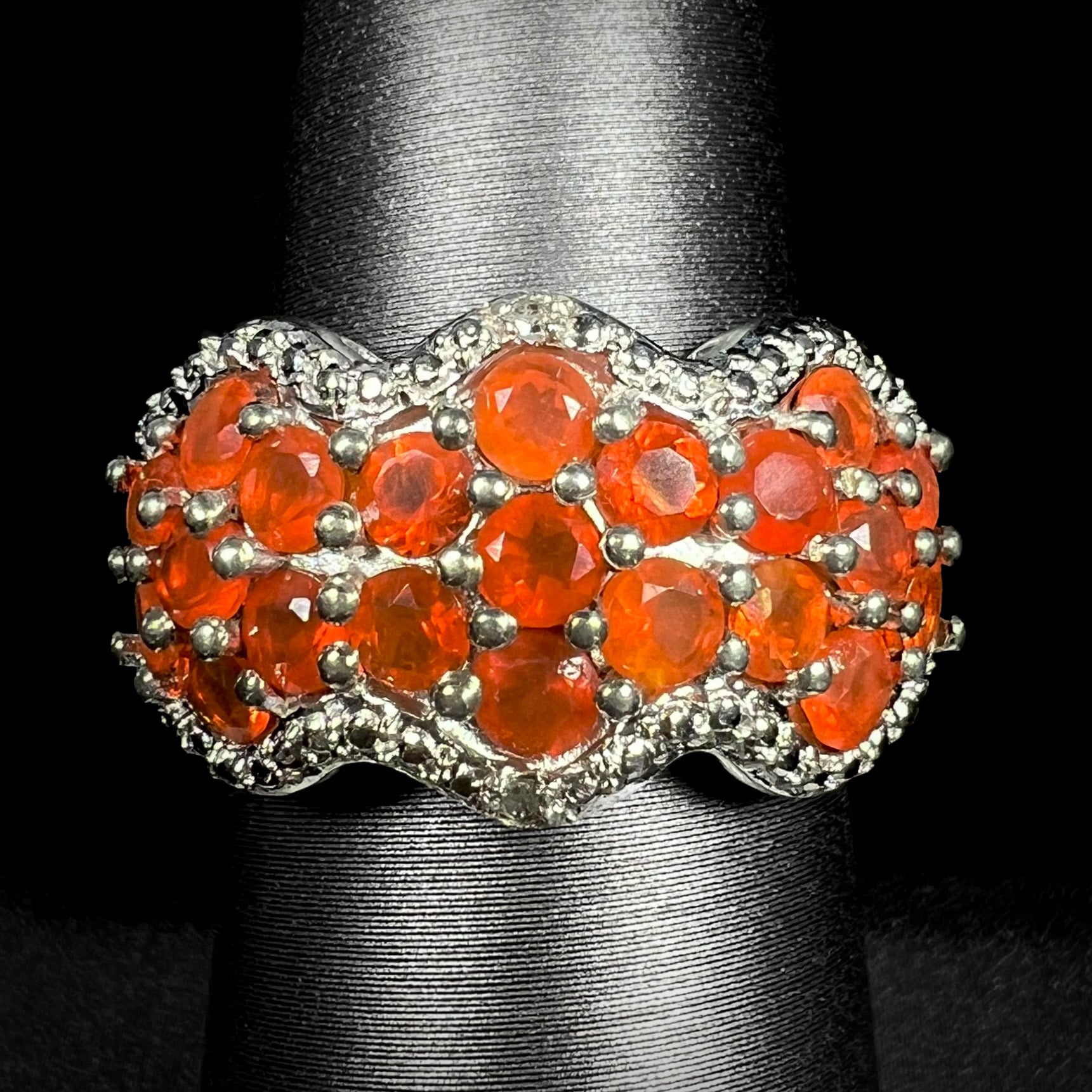 Front close-up of a Mexican fire opal cluster ring with diamond accents in sterling silver, shown on ring display against black background.