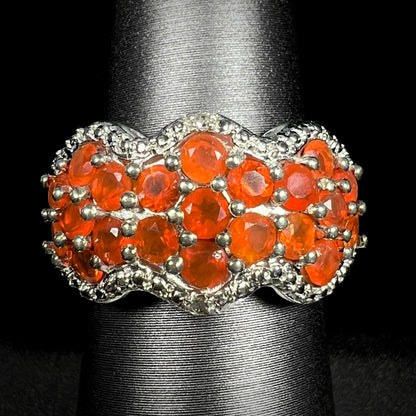 Front close-up of a Mexican fire opal cluster ring with diamond accents in sterling silver, shown on ring display against black background.